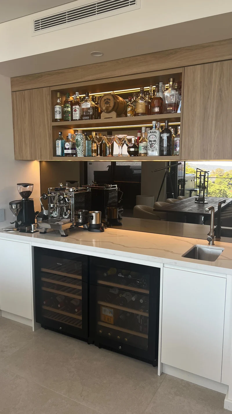 Bronze mirrored splashback behind a coffee machine and sink in a timber home bar
